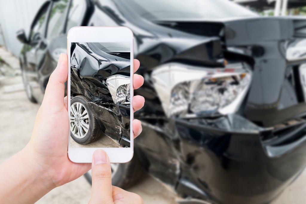 female hold mobile smartphone photographing car accident - Travis Legal Offices | Colorado Personal Injury Law Firm