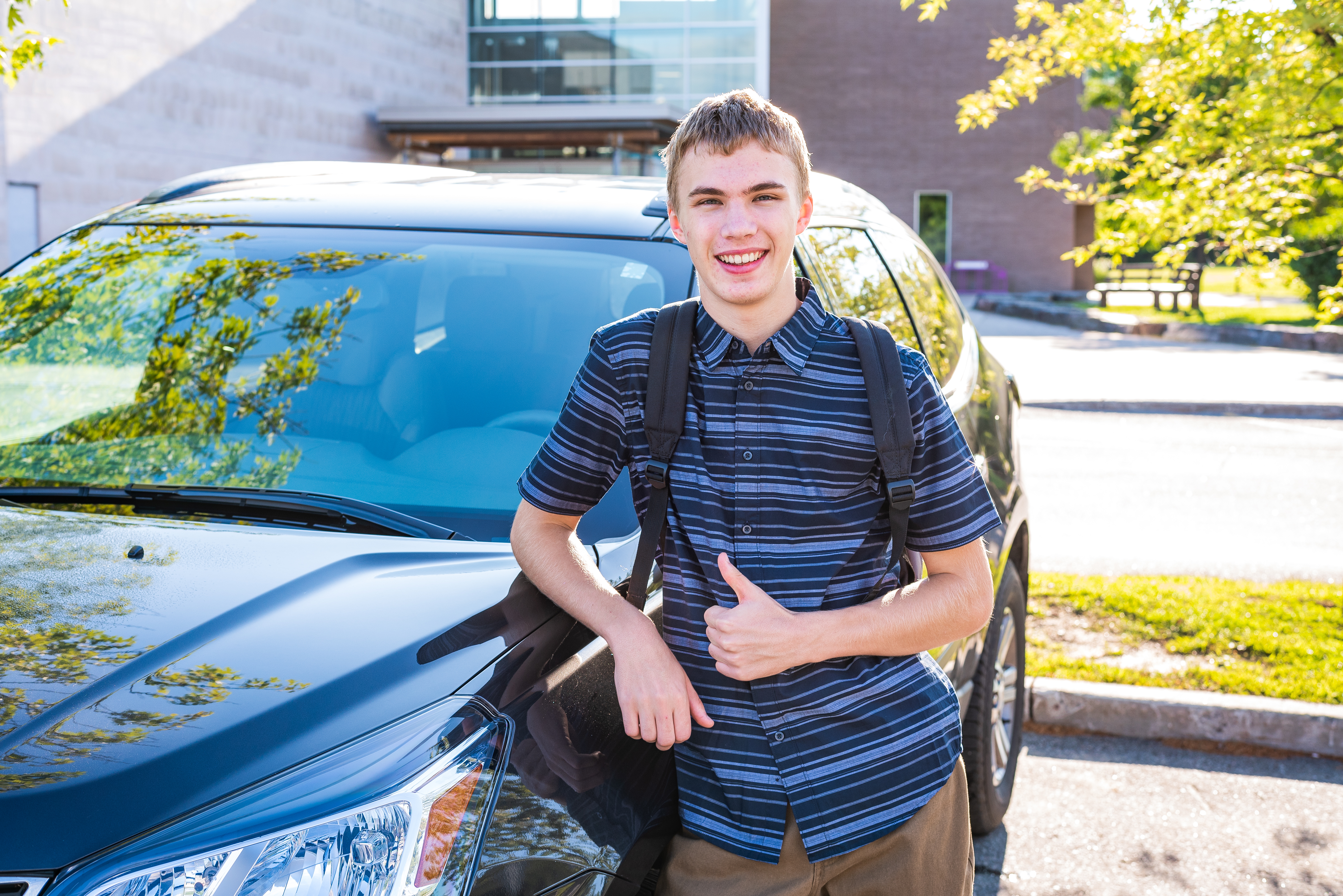 Happy male teenager leaning against his car in a high school parking lot - Travis Legal Offices | Colorado Personal Injury Law Firm