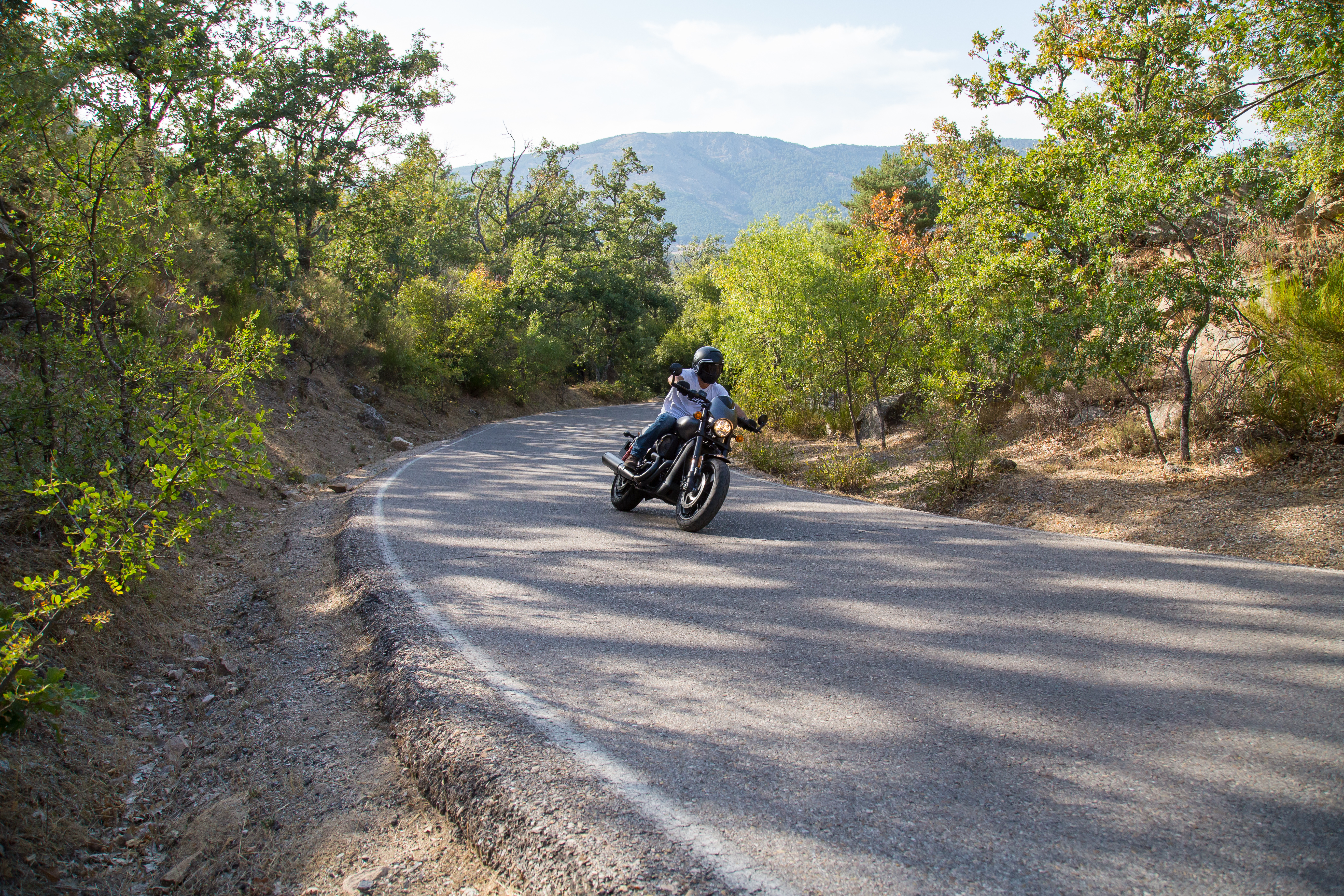 Young man riding a motorcycle on road turning in a curve in the mountains on sunny day