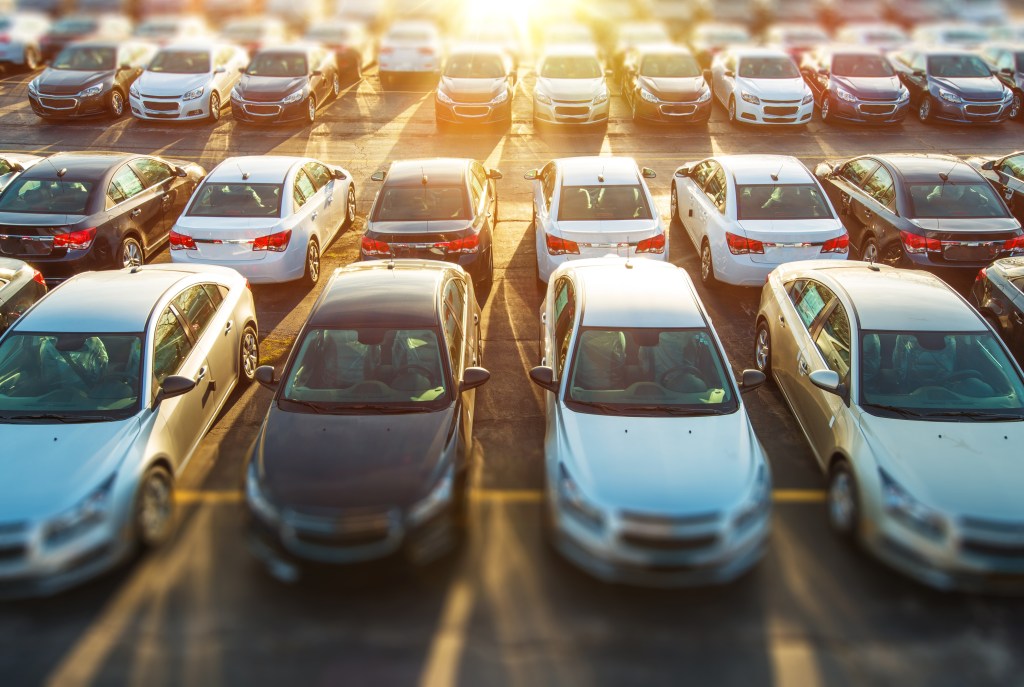 Aerial view of a crowded parking lot filled with silver and white sedans parked in neat rows at sunset.