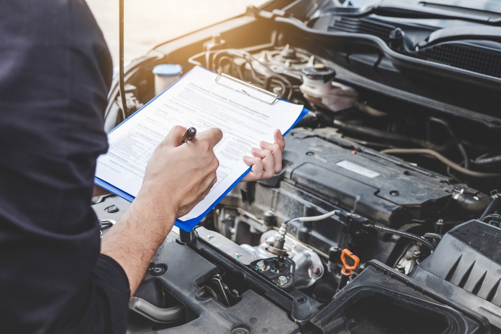 Services car engine machine concept Automobile mechanic repairm - Travis Legal Offices | Colorado Personal Injury Law Firm Person in a dark sleeve writes on a clipboard under an open car hood, inspecting the engine area.